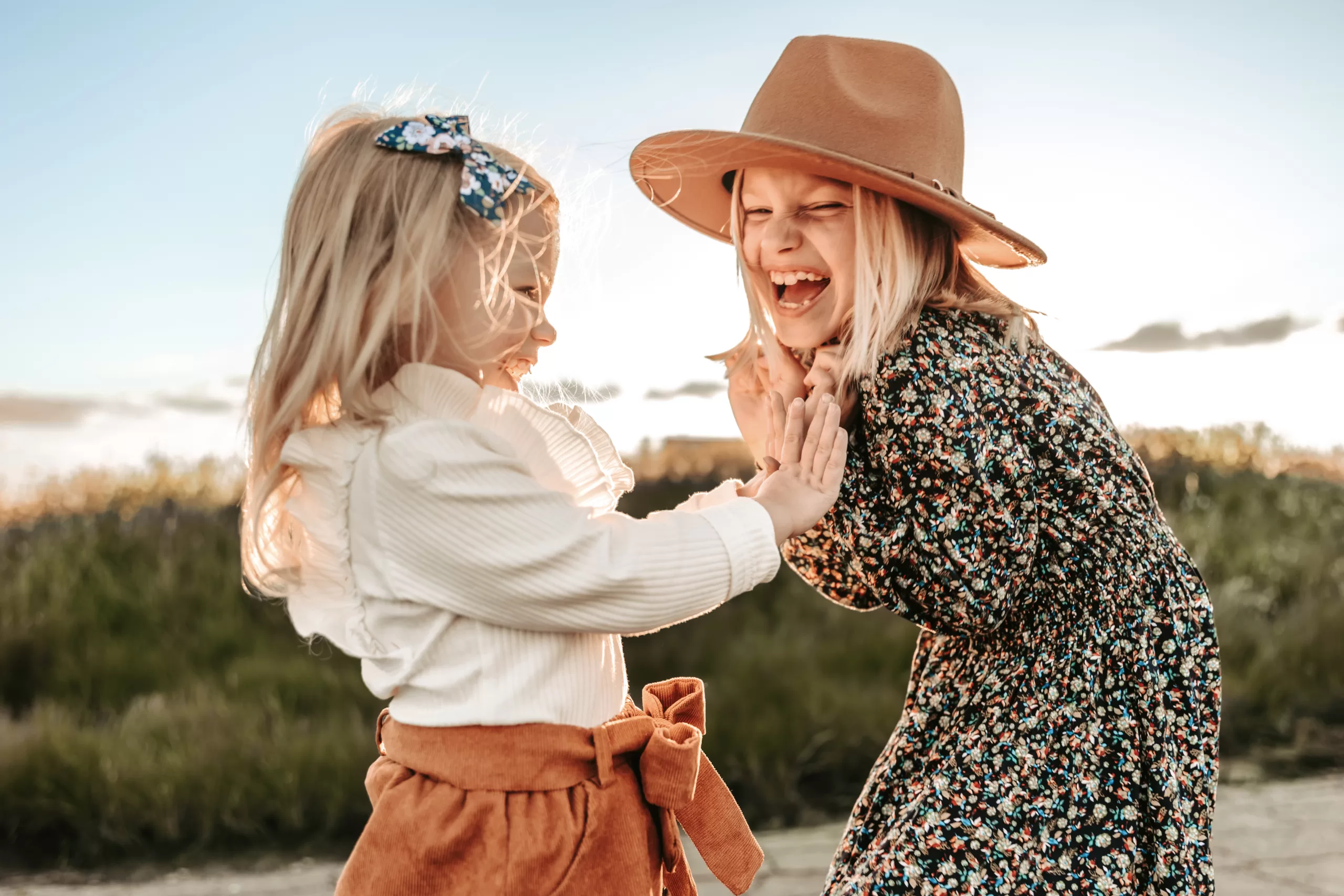 two girls clapping and smiling in front of a green field of mustard flowers